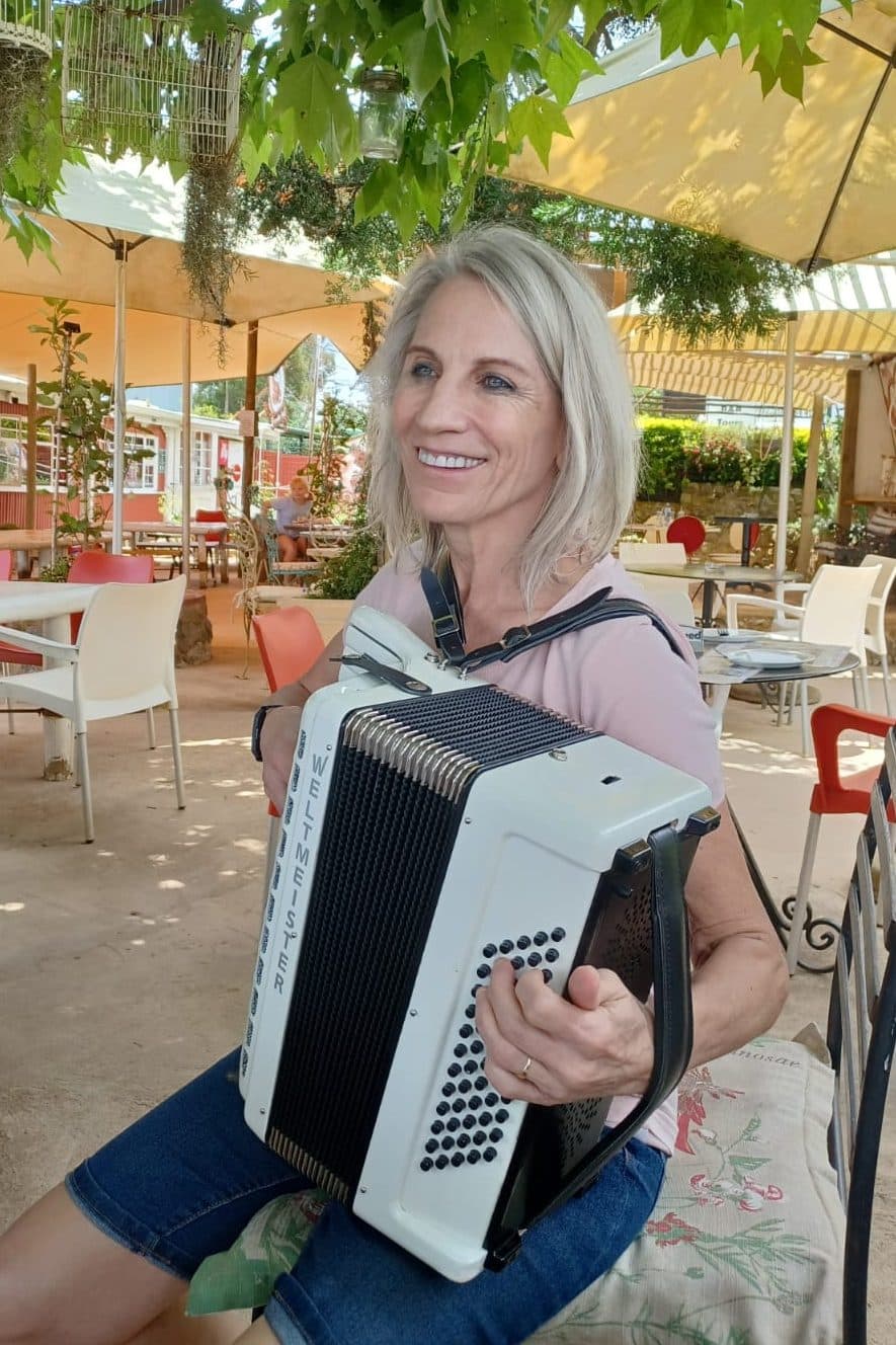 Esmé Bergh holding her accordion on a shaded restaurant terrace