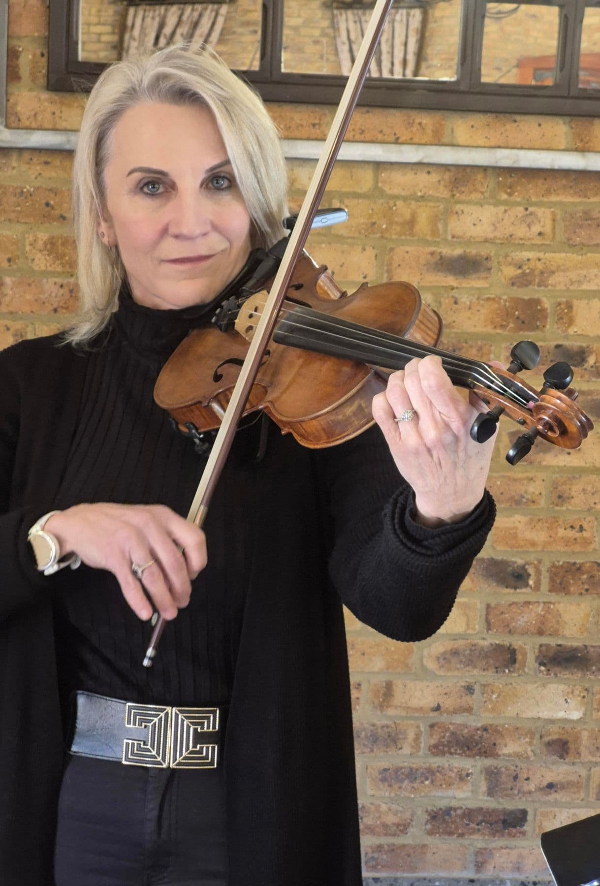 Esmé Bergh playing the violin, bow raised, looking straight at the camera, against a brick wall