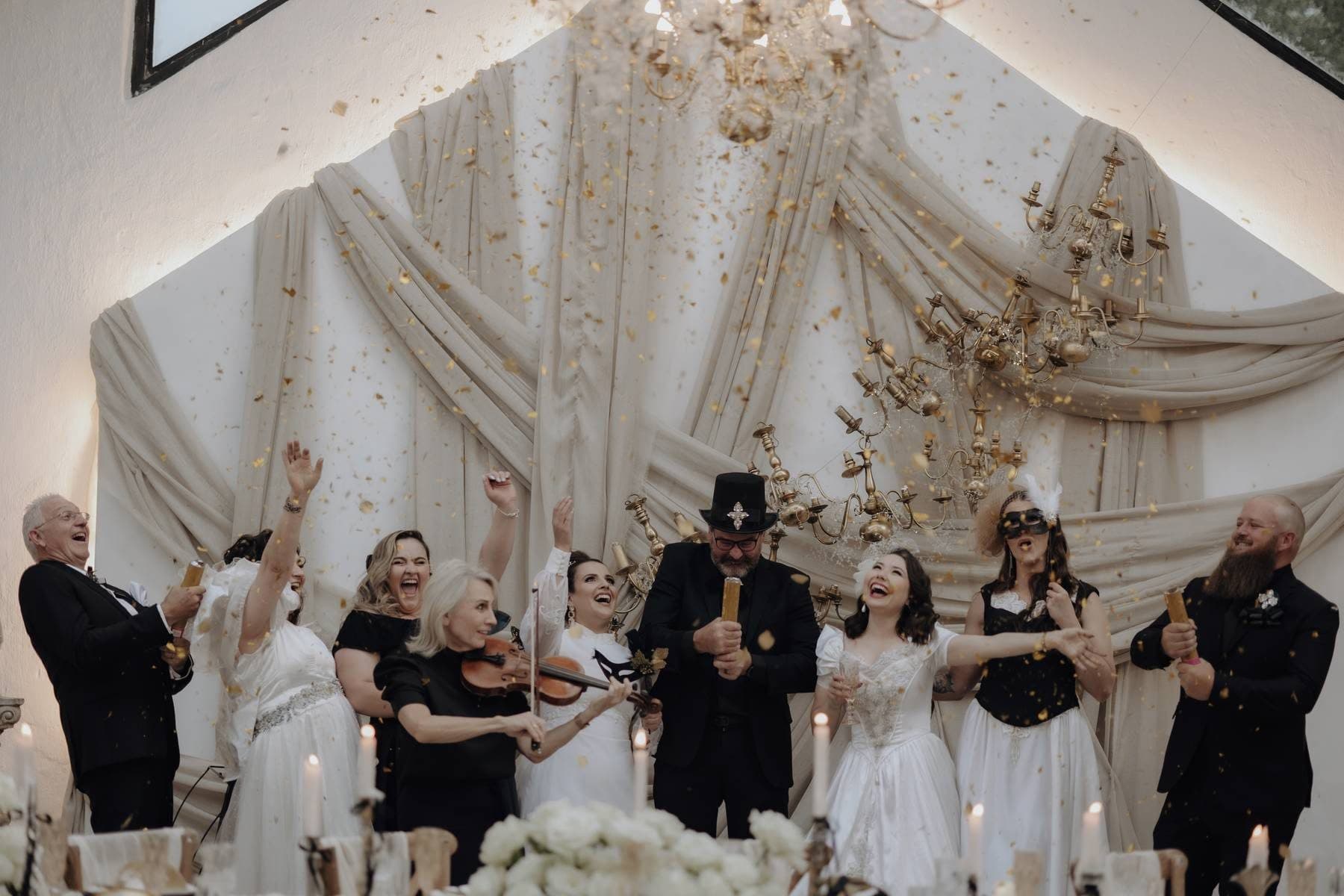 A wedding party celebrating under a draped cream and gold arch lit by candles