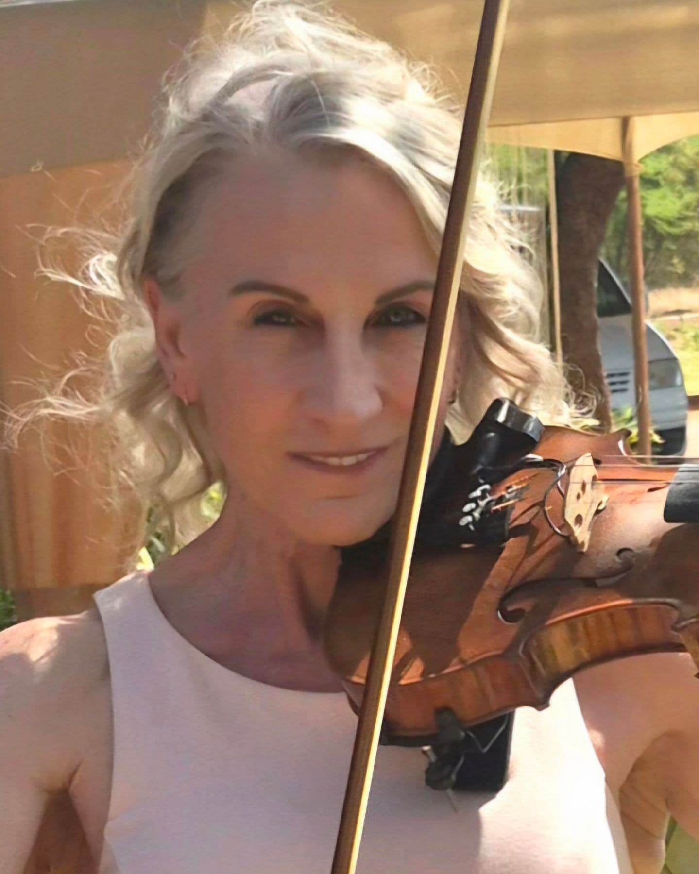 A close view of Esmé Bergh playing the violin outdoors, her bow crossing in front of her face