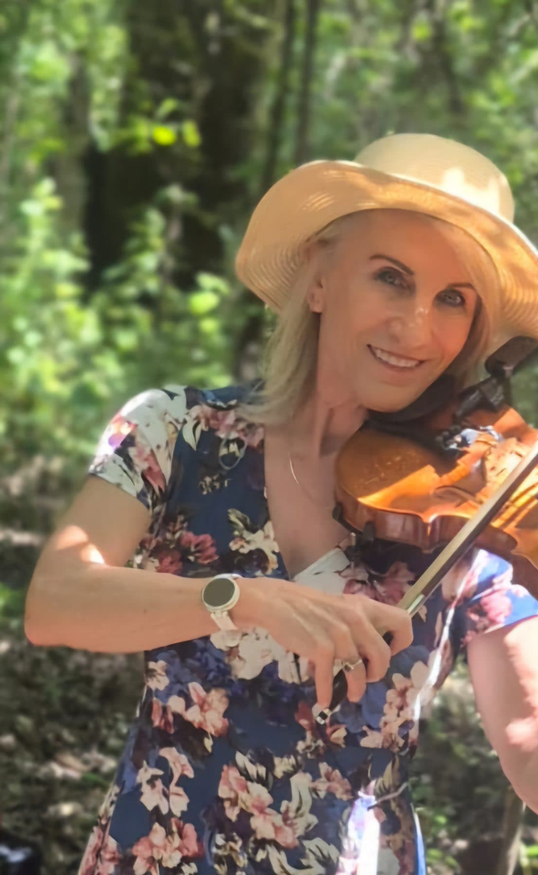 Esmé Bergh playing the violin among trees, wearing a wide straw sun hat