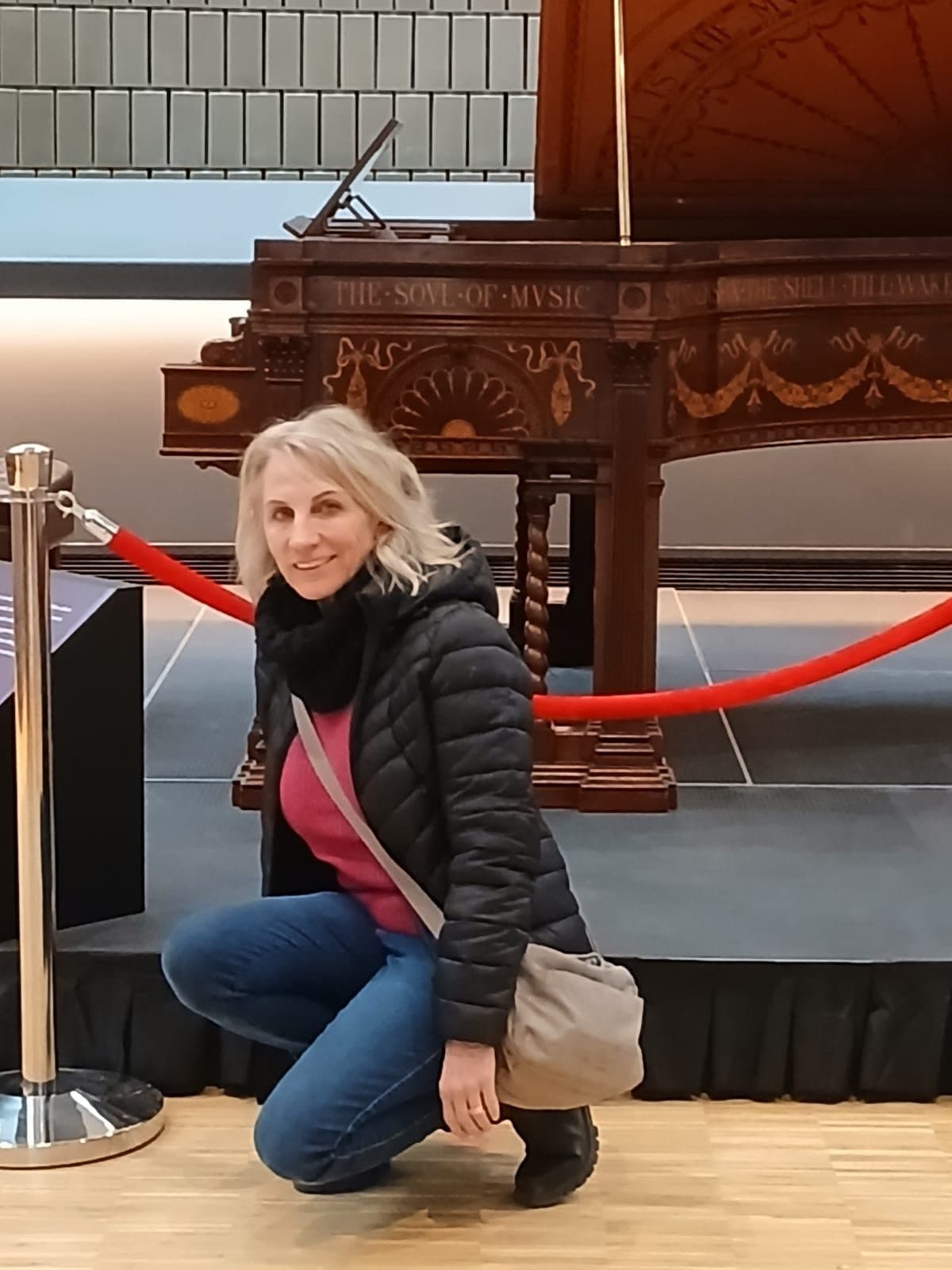 Esmé Bergh kneeling beside an ornate antique grand piano behind a rope barrier in Canada