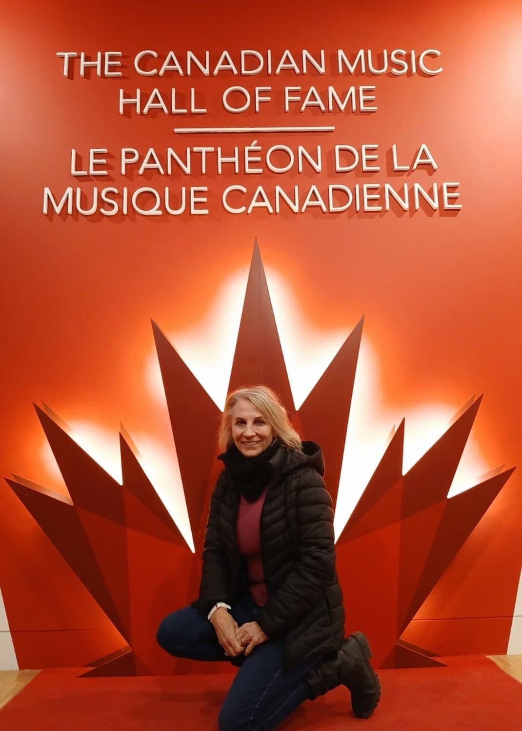 Esmé Bergh kneeling in front of the Canadian Music Hall of Fame display