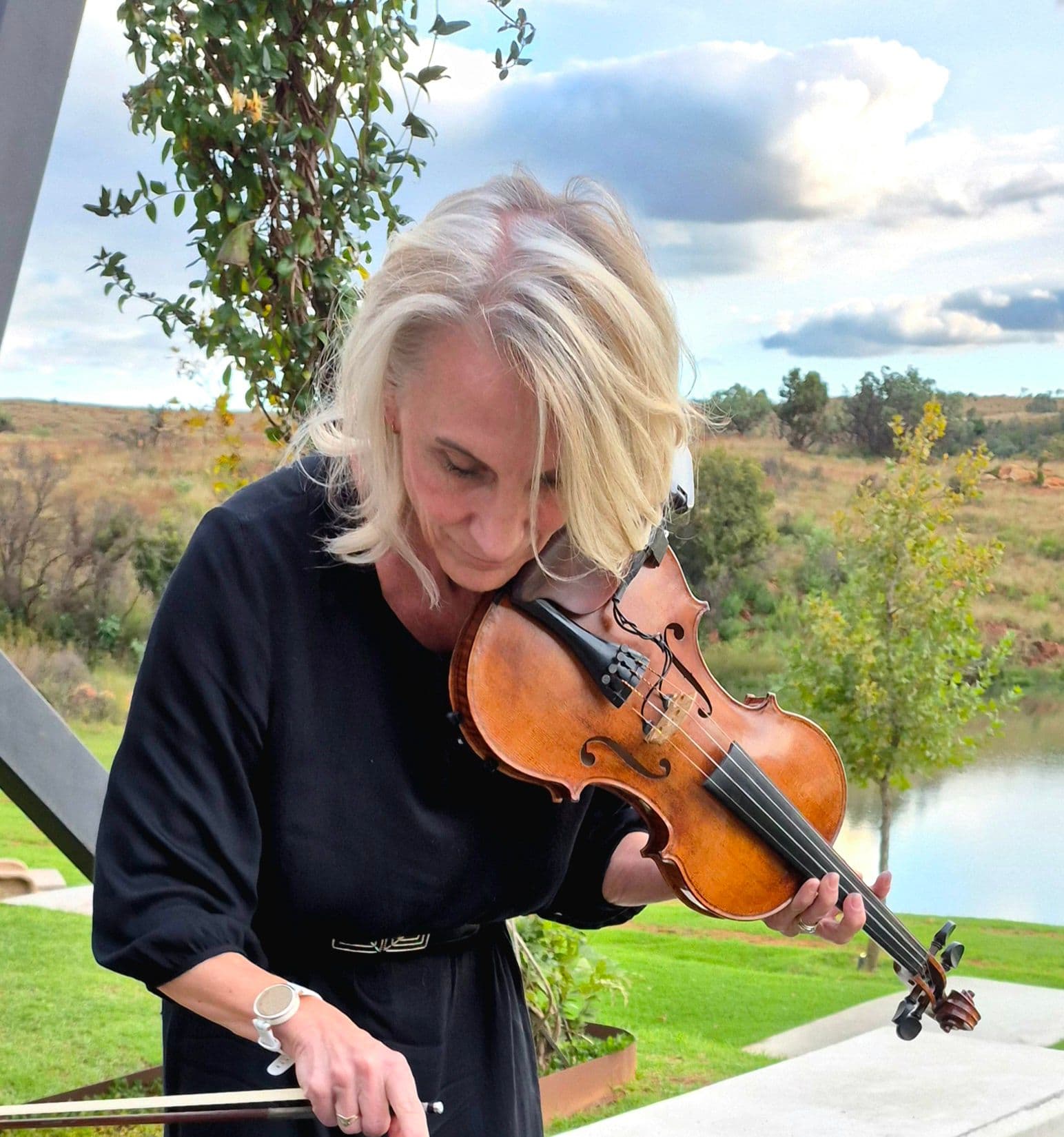 Esmé Bergh playing the violin outdoors in late afternoon light, a lake and open veld behind her