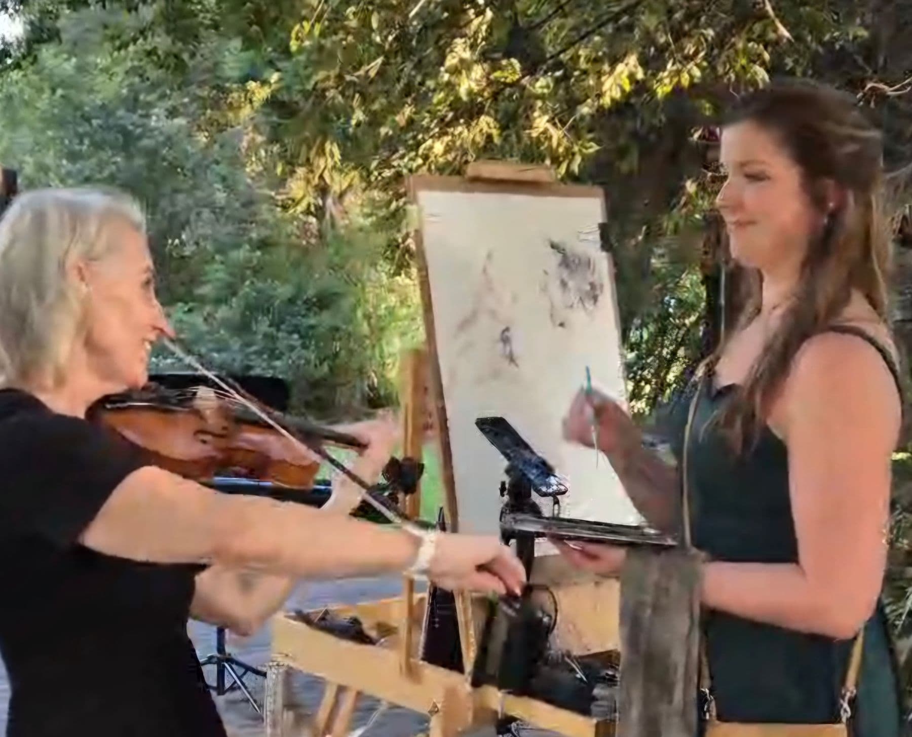 Esmé Bergh playing the violin outdoors beside a painter working at an easel