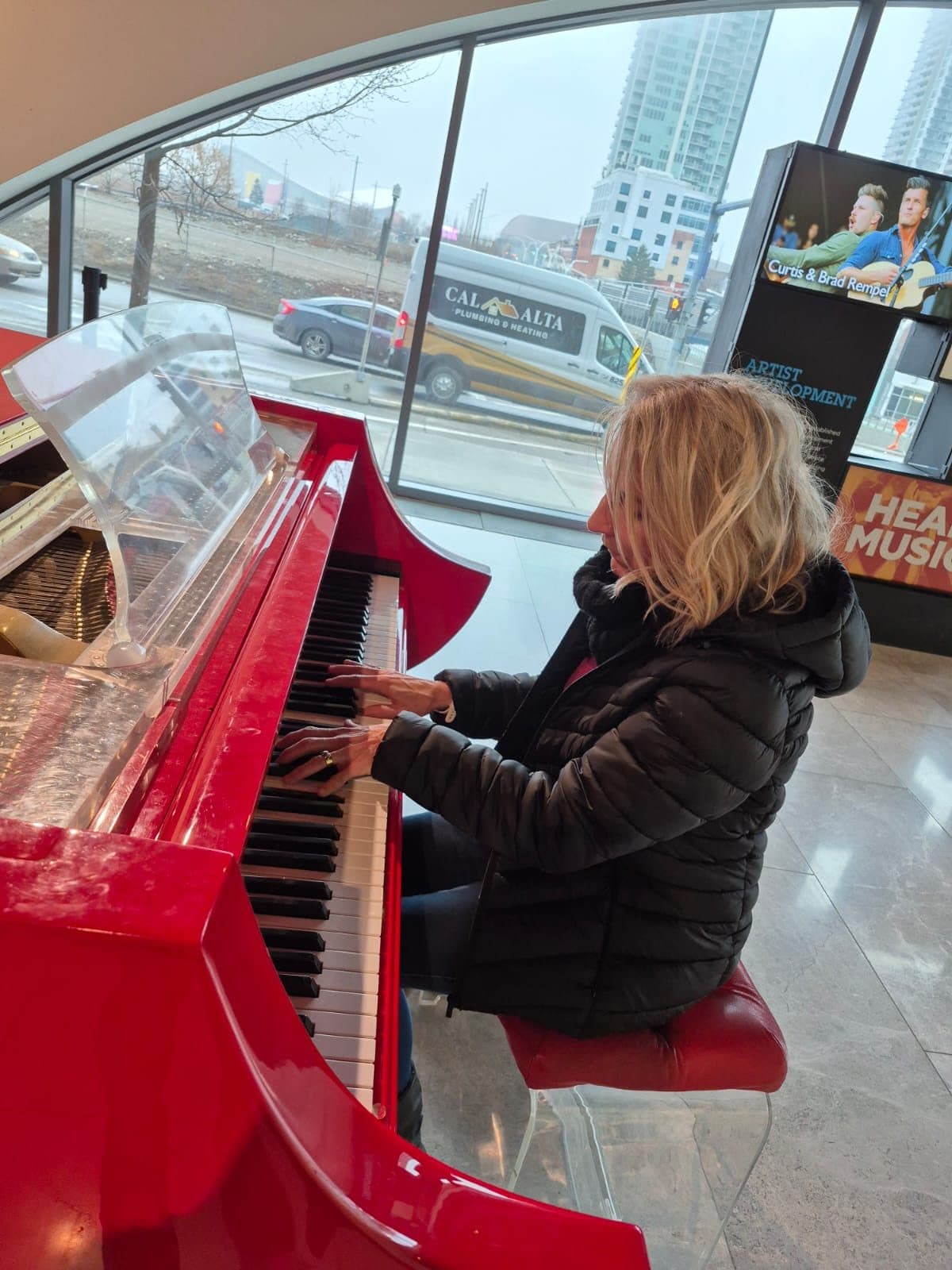 Esmé Bergh playing a red grand piano in a glass-fronted building in Canada