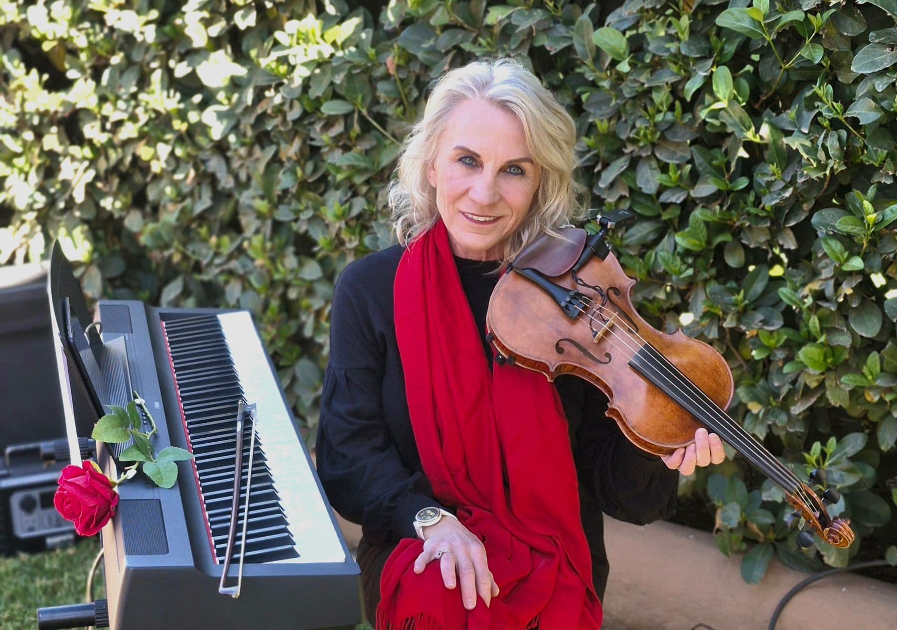 Esmé Bergh in a red scarf, holding her violin beside a digital piano with a red rose resting on it