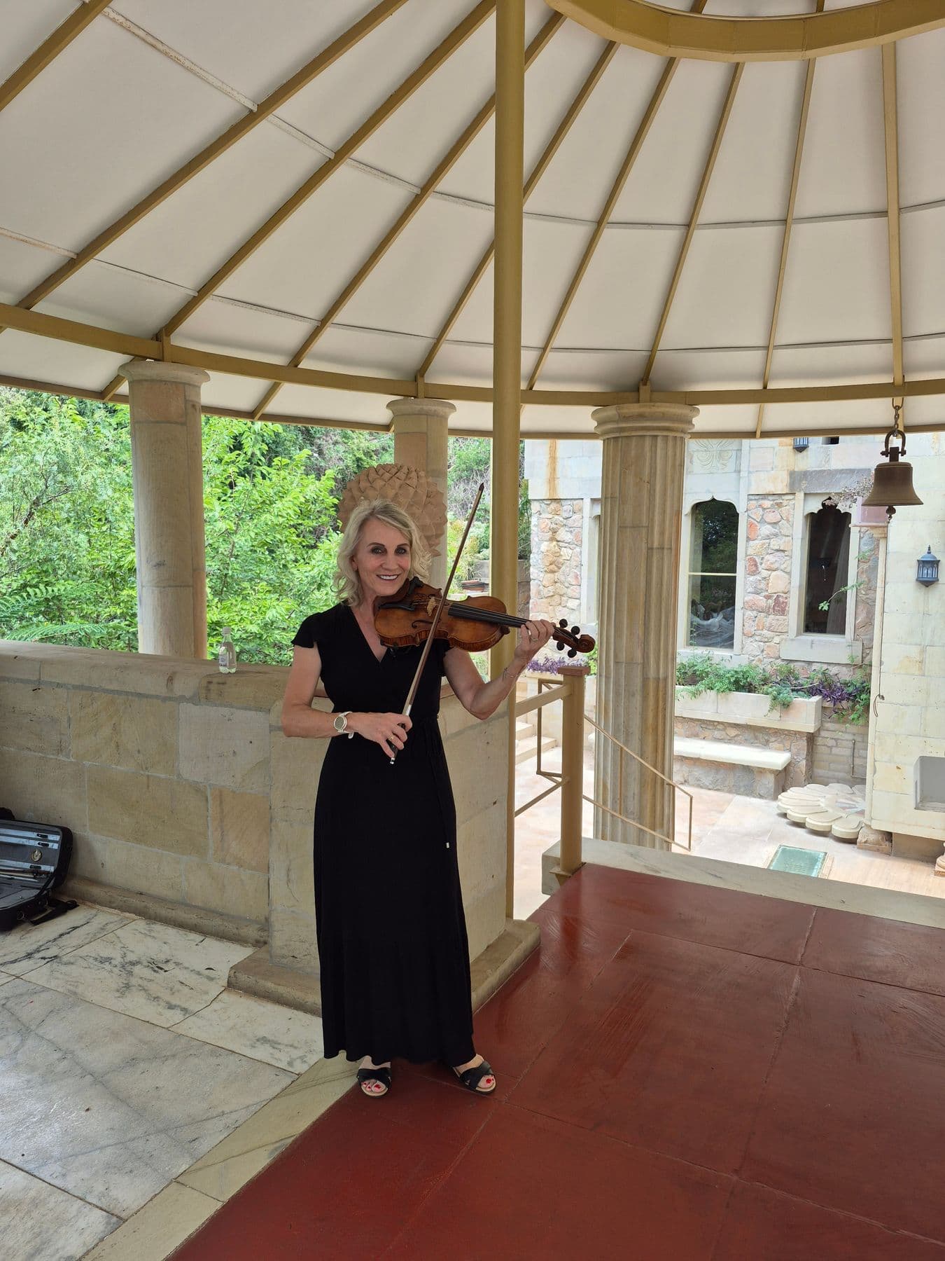 Esmé Bergh in a long black dress playing the violin under a white canopied rotunda with stone columns