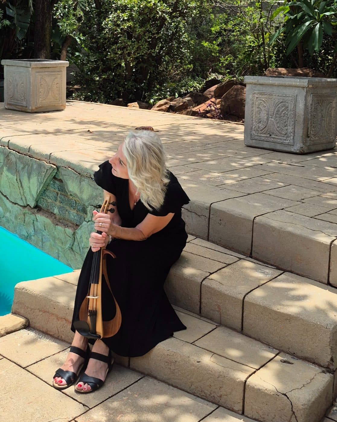 Esmé Bergh sitting on garden steps beside a pool, holding her violin