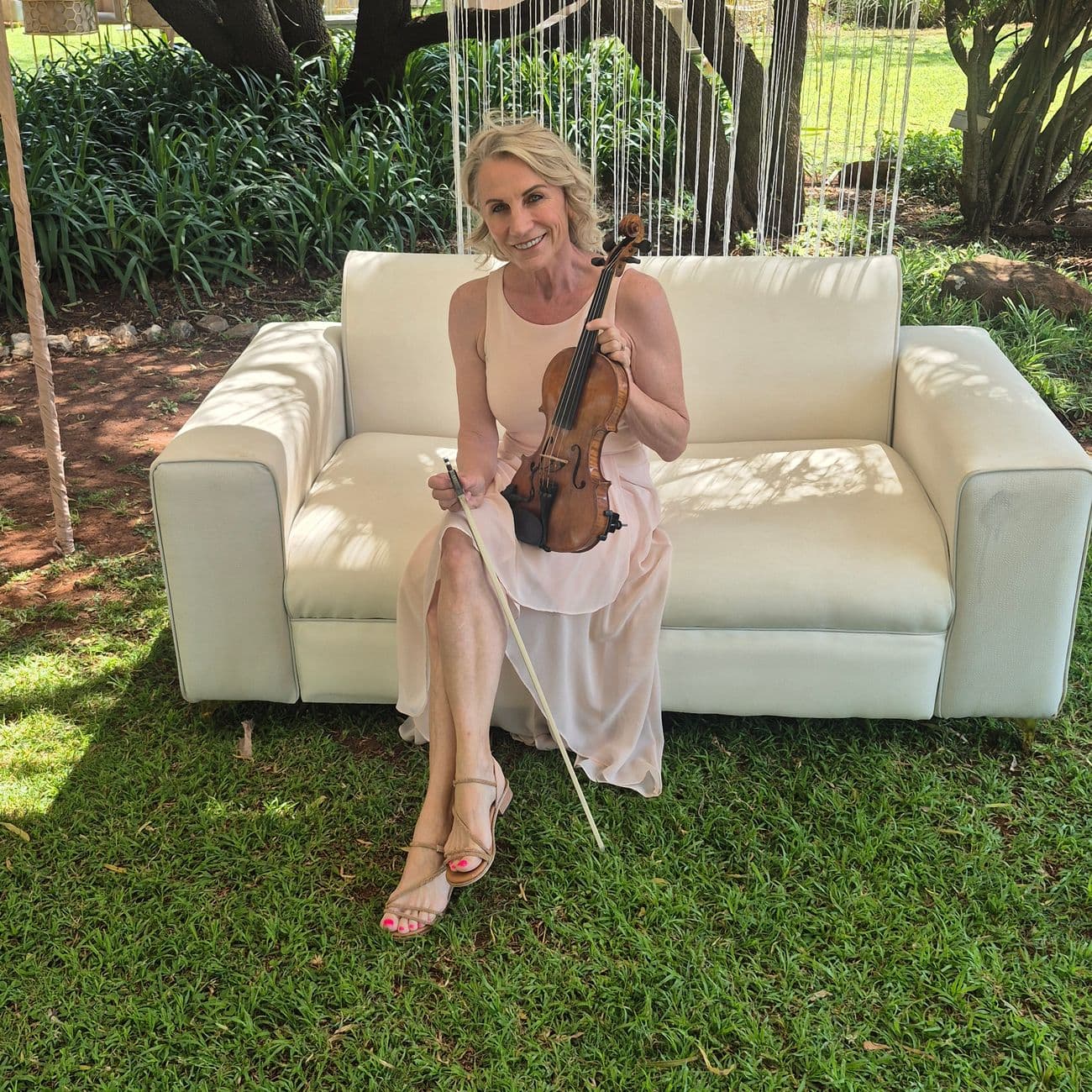 Esmé Bergh seated on a cream sofa on a lawn, her violin resting across her lap and her bow in her hand